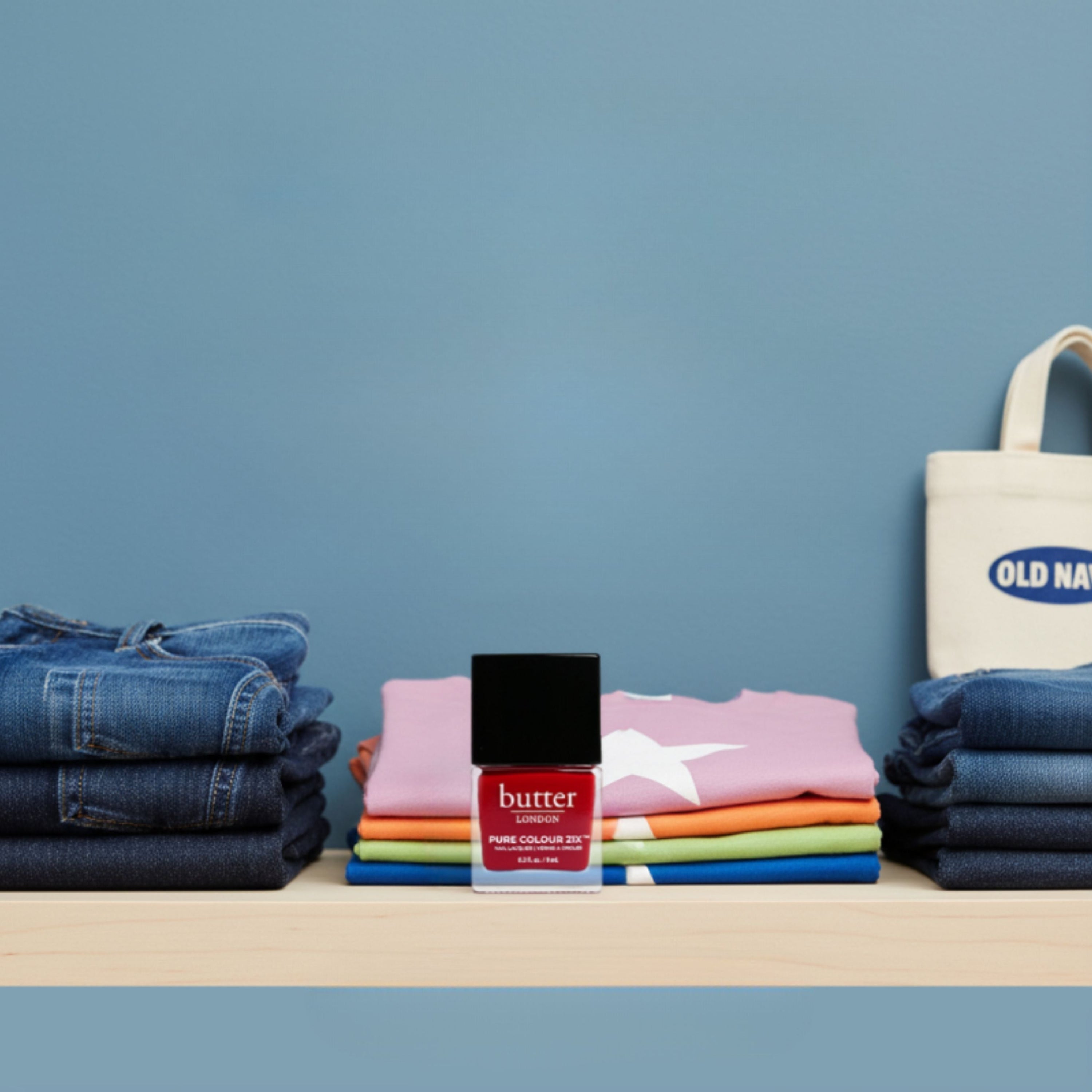 Butter London nail polish with stacked colorful tees and an Old Navy bag against a blue background.