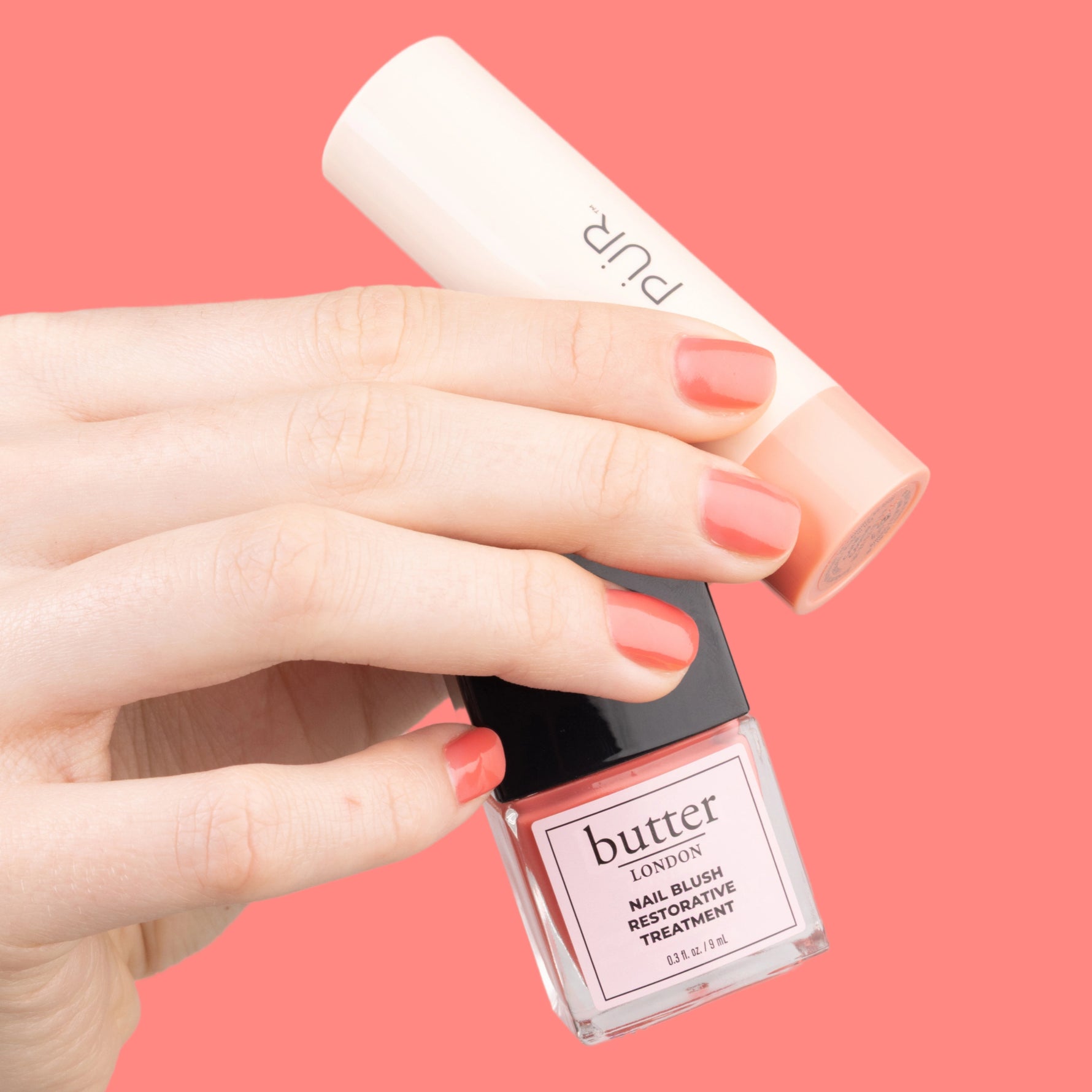 PÜR x butter LONDON Blush Crush - hand holding Sunset Glow Nail Blush and Coral Cosmo Silky Tint against coral background