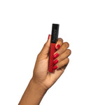 Hand holding red Plush Rush Lip Gloss Siren tube with black cap against white background.