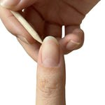 Wooden dual sided cuticle pusher held between fingers near the nail showing beveled edge and pointed tip