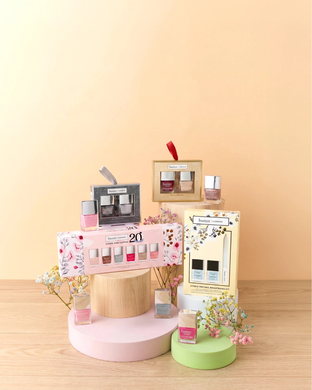 Extra Something Deal: 20% Off Kits and Sets - Various butter LONDON nail lacquer and nail care sets on varying pillars sitting on wooden surface with neutral gradient background (mobile - focal point)
